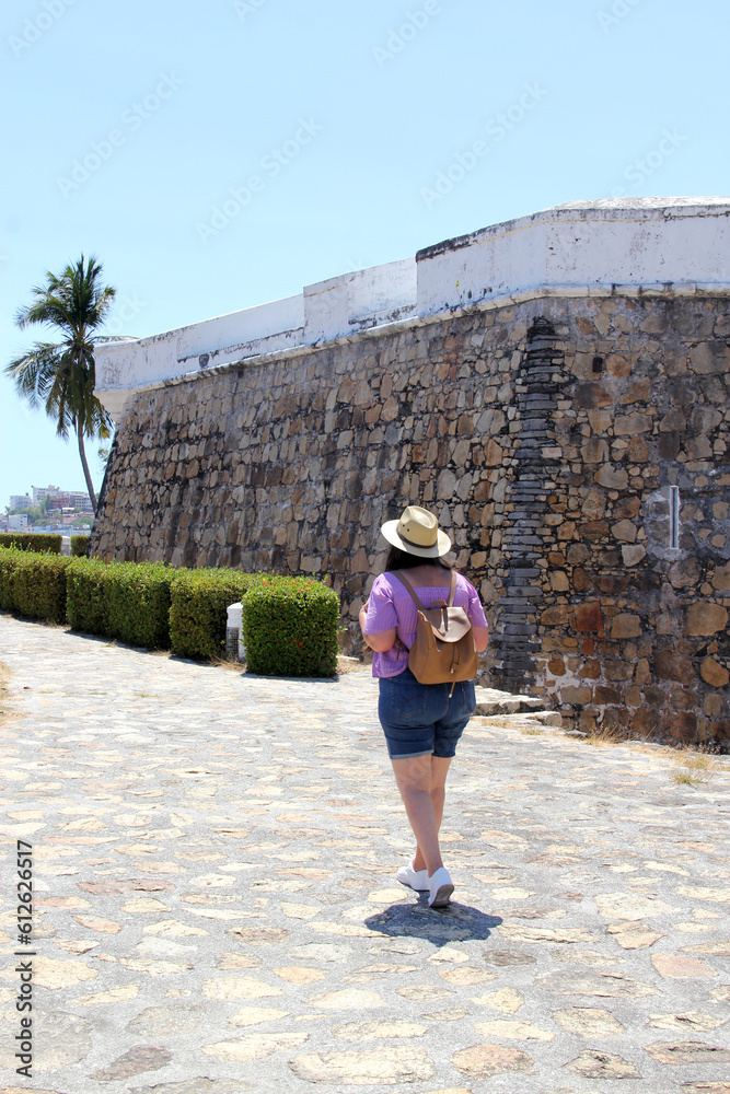 Adult Latina woman wearing sunglasses and sombrero walks the historic streets of Acapulco, Guerrero, Mexico as a tourist exploring