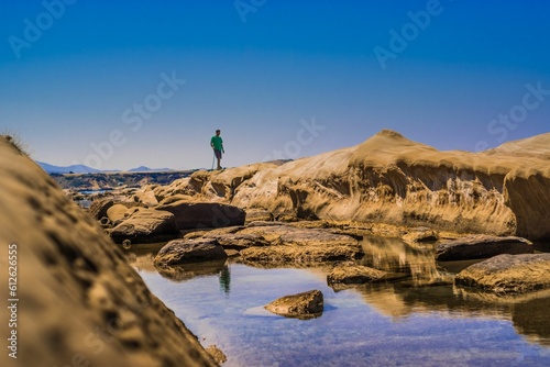 Person standing on the big rocks reflected in the water puddle against the blue sunny sky