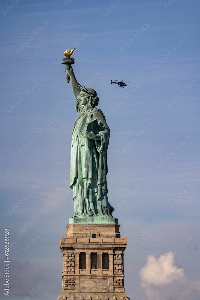Fototapeta premium Statue of Liberty on a sunny day, with a helicopter flying in the blue sky in the background