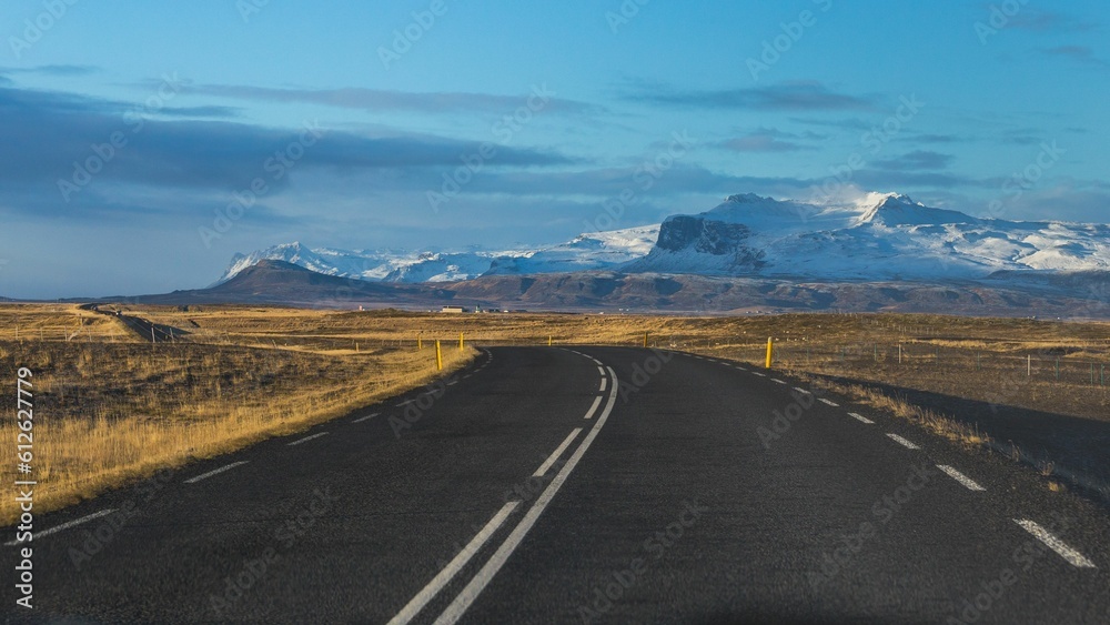 Empty road surrounded by fields with snowy mountain in the background