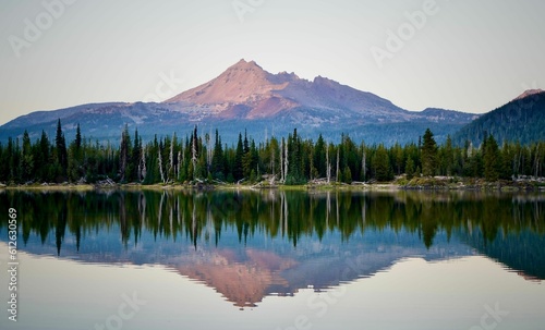 Scenic view of a lake reflecting green forests and mountains on its shore at sunset