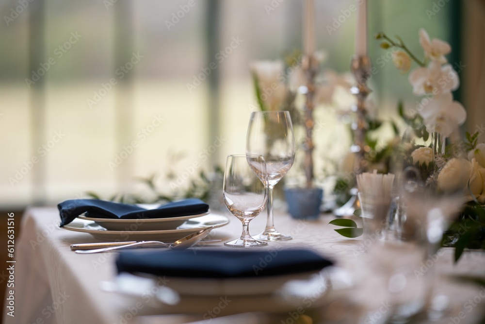 Fototapeta premium Closeup of a festive table with white dishes and glasses, blurred background
