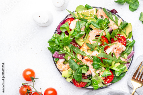 Fresh salad with avocado, shrimps, red tomatoes, arugula, lamb lettuce, red onion and sesame seeds on white table background. Top view