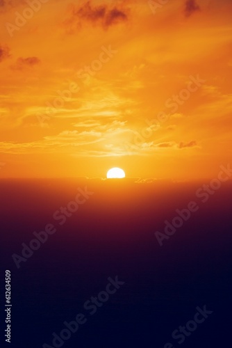 Fototapeta Naklejka Na Ścianę i Meble -  orange sunset seen through the clouds illuminating the sky and reflecting off of the ocean below