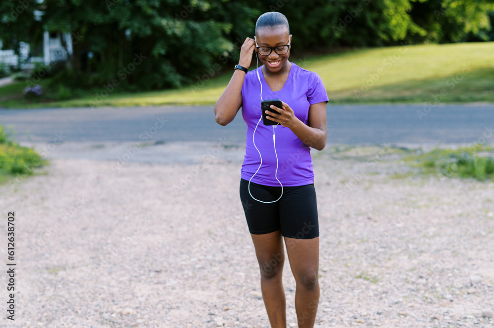 Young black teen in active wear holding phone, wearing headphones Young black teen in active wear holding phone, wearing headphones