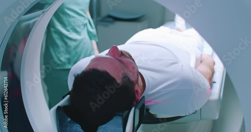 Close-up back shoot of male patient undergoing tomography examination. Man is going into MRI machine. Doctor is performing procedure. Patient is moving at scanner bed. Tomography under infrared rays.