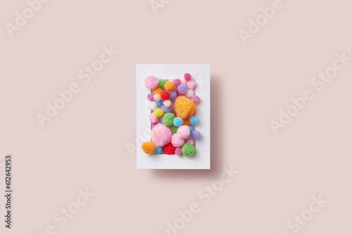 Colorful fluffy pompons in white paper frame.