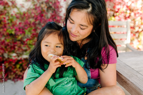 Asian mom sitting outdoors with her children who are eating a snack photo