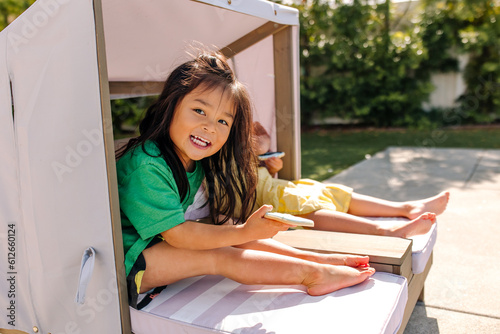 Happy asian kids sitting on a patio outdoor chaise with sun protection photo