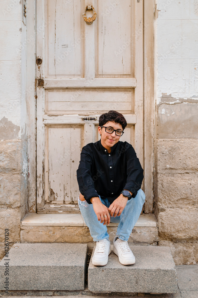 Young transgender man posing sitting on the front steps of a house.