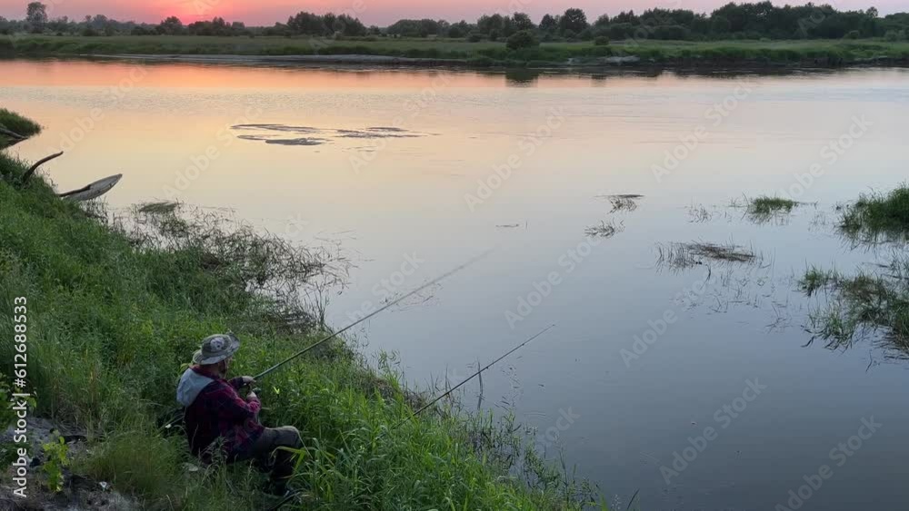 A man is fishing on the banks of a large river. A man is fishing on the banks of a large river.
