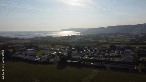 Aerial rising view Welsh caravan park at sunrise overlooking shimmering coastal bay and rolling countryside hills photo