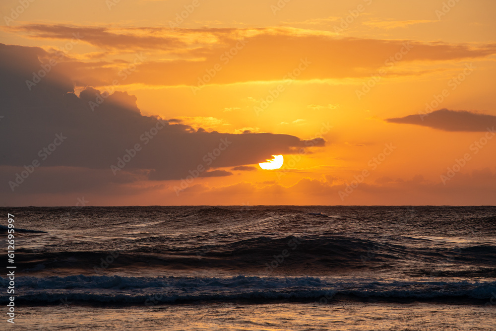 Sunset Behind Clouds with Waves Breaking on Beach in Kauai Hawaii