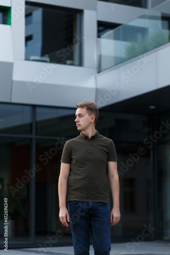 young man in a green t-shirt, jeans, and sandals on a campus