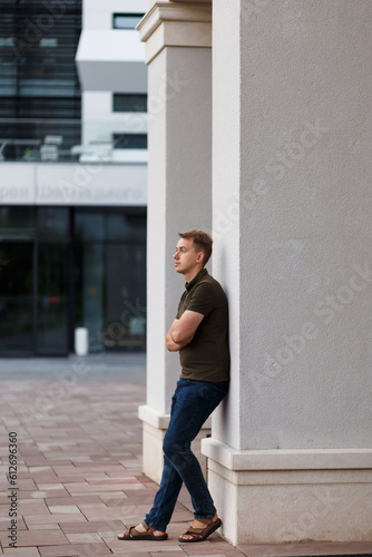 young man in a green t-shirt, jeans, and sandals on a campus