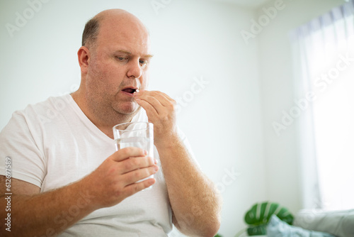 Handsome senior man holding a glass of water and taking a pill while lying on bed at home. Home health care.