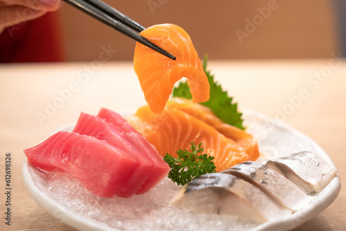 Eating a freshness raw salmon sashimi fillet piece by using chopsticked picking-up. Japanese food object, close-up and selective focus.