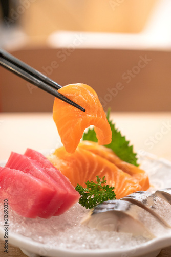 Eating a freshness raw salmon sashimi fillet piece by using chopsticked picking-up. Japanese food object, close-up and selective focus.