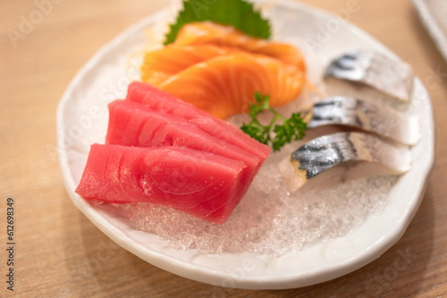Set of raw freshness sashimi in various sliced kind of fishes are served in white ceramic bowl and placed on wooden table. Japanese food meal photo, selective focus.