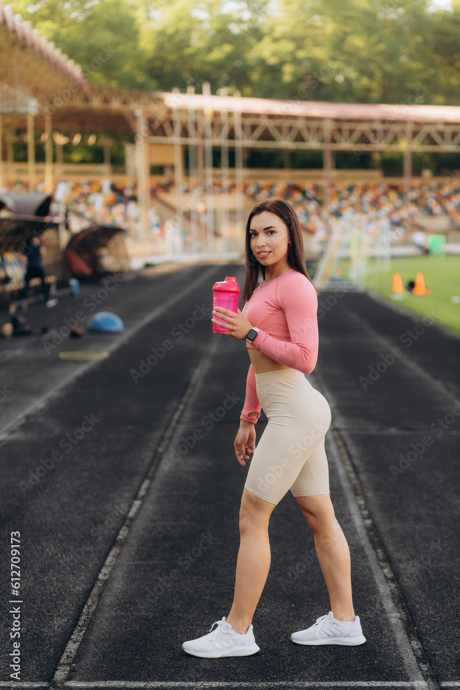 Tired Woman drink water red bottle after morning workout. Young athletic femalestanding city street background after jogging Healthy lifestyle concept.