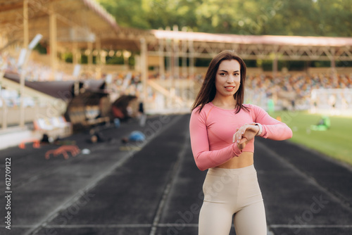 Portrait of athletic attractive woman in sportswear standing at the football stadium and looking on the indicators on her sport watch, healthy lifestyle.