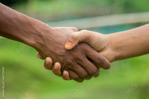 A white man and a black man shake hands together with each other with their hands and the background behind them is blurred © Rokonuzzamnan