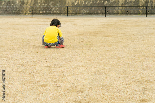 公園のグラウンドで一人座り込む小さな子供。いじける男の子。