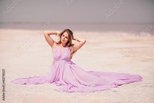 Pink lake woman. A woman in a pink dress sits on the salty shore of a pink lake and poses for a souvenir photo, creating lasting memories.