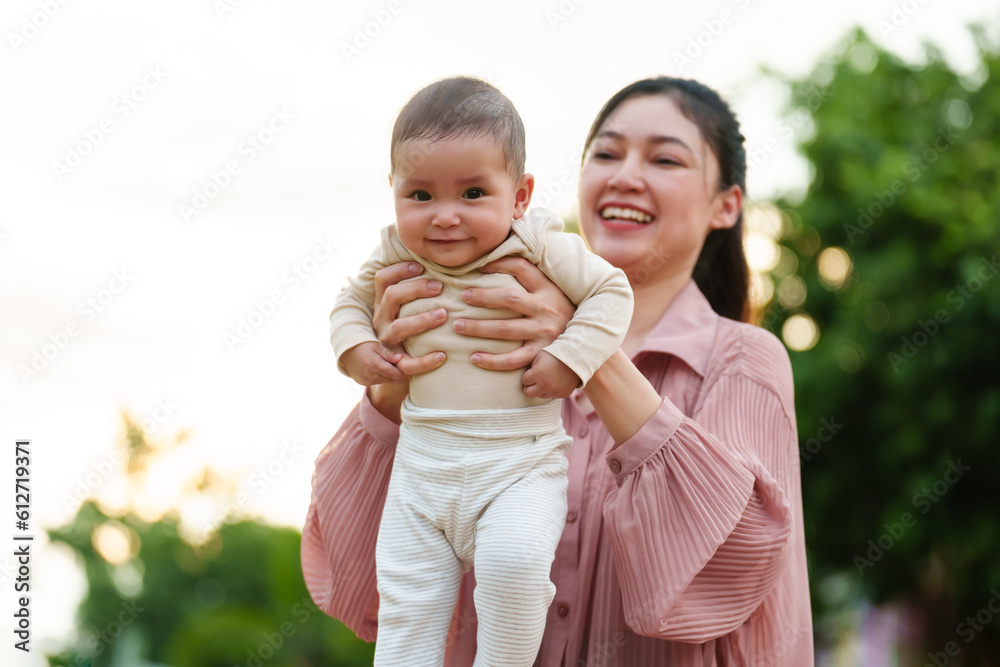 Fototapeta premium mother holding and lifting with her baby newborn in park with sunlight.