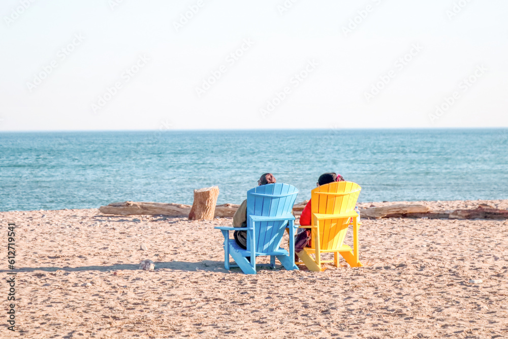 Two women sitting on colorful wooden beach chairs overlooking Lake Ontario, Canada Two women sitting on colorful wooden beach chairs overlooking Lake Ontario, Canada