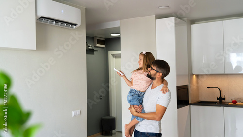 Father with little daughter on hands turn on air conditioner using remote control. Happy family adjust comfortable temperature of cooler system