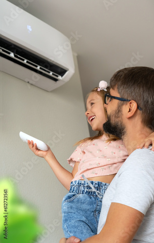 Happy family, father and little daughter fun turn on air conditioner using remote control.