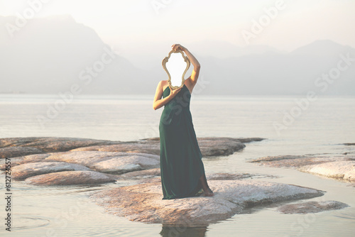surreal woman holding mirror in front of her face in amazing natural scene , abstract concept photo