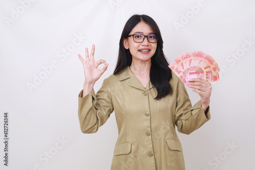 Happy young government employee holding indonesian banknotes while showing okay hand gesture photo