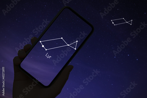 Woman using stargazing app on her phone at night, closeup. Identified stick figure pattern of Lyra constellation on device screen