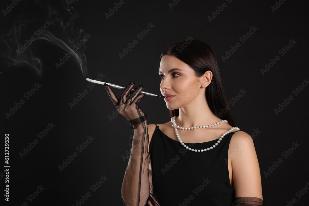 Fototapeta premium Woman using long cigarette holder for smoking on black background, space for text