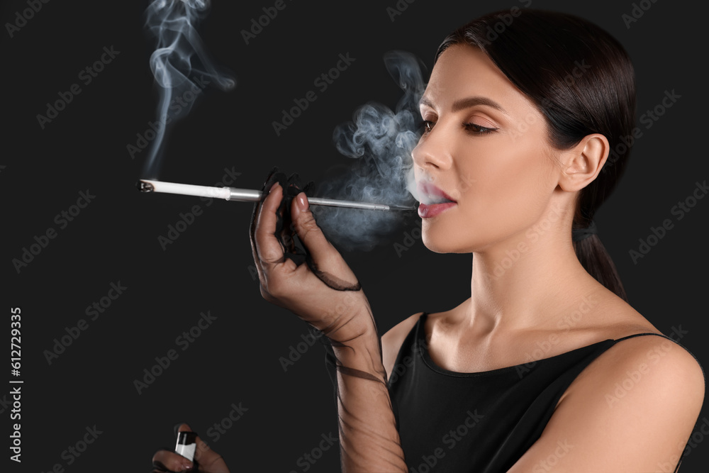 Fototapeta premium Woman using long cigarette holder for smoking on black background
