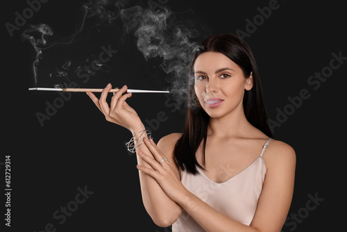 Woman using long cigarette holder for smoking on black background
