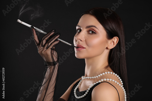 Woman using long cigarette holder for smoking on black background