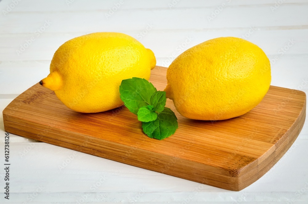 Yellow fruits with green leaves on a wooden board. Lemons on chopping board on white wooden table.
