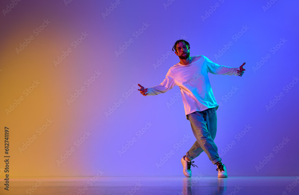 Dance show. Young guy dancing contemp, breakdance and hip-hop against gradient multicolored studio background in neon light