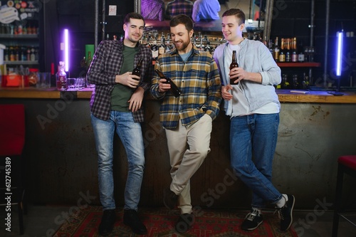 Friends having fun. Happy young men in casual wear drinking beer in pub.