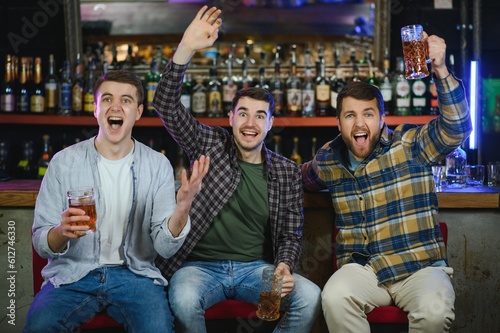 Soccer fans cheering for favourite team while enjoying drinks. Group of supporters celebrating victory while watching football match on tv in a club. Happy friends shouting while cheering for a goal.