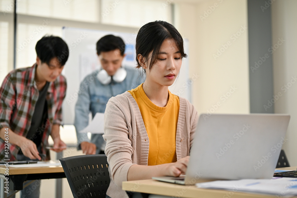 A focused young Asian female marketing assistant is working on her work on her laptop A focused young Asian female marketing assistant is working on her work on her laptop