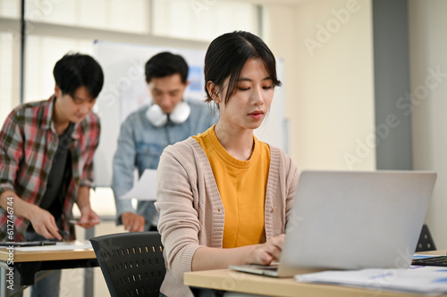 A focused young Asian female marketing assistant is working on her work on her laptop