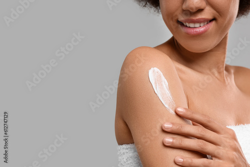 Photography Young woman applying body cream onto arm on grey background, closeup