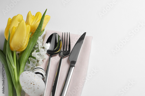 Cutlery set  Easter eggs and beautiful flowers on white background  flat lay with space for text. Festive table setting
