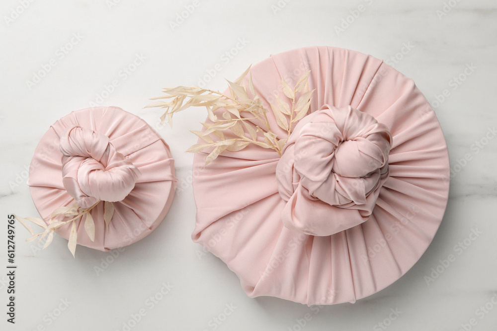 Obraz premium Furoshiki technique. Gifts packed in pink fabric and dried branches on white marble table, flat lay