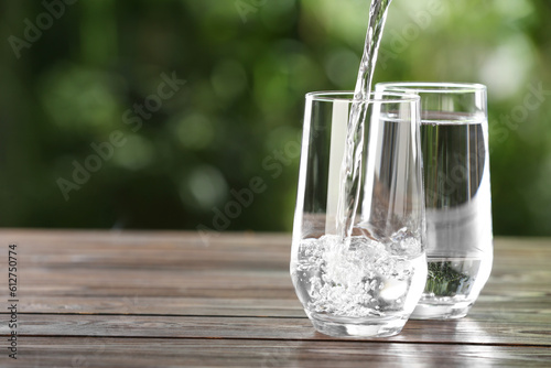 Pouring water into glass on wooden table outdoors, space for text