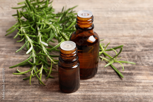 Bottles of essential oil and fresh rosemary sprigs on wooden table